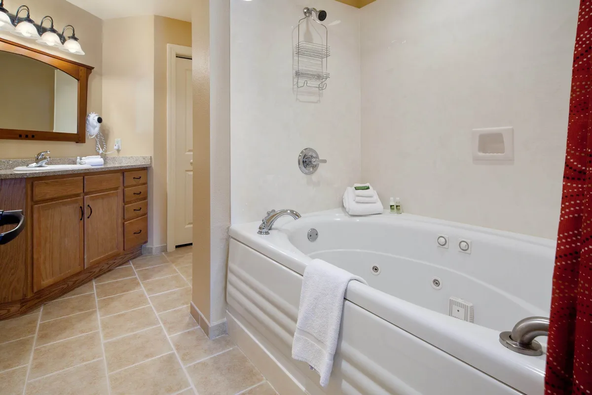An oversized in-room jacuzzi spa tub, paired with a vanity and wooden cabinetry, creates a tranquil bathroom retreat designed for relaxation and rejuvenation.